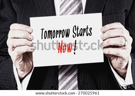 A businessman holding a card with the words,  Tomorrow Starts Now! written on it.