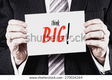 A businessman holding a card with the words, Think Big! written on it.