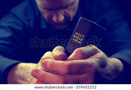 A Man praying holding a Holy Bible.