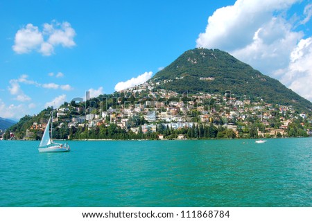 View of mountain from lake Lugano, Switzerland. Panorama, sunny day, lake with sailing boat.Travel, relax