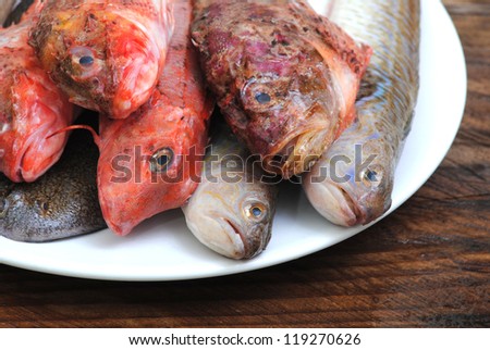 Fresh fishes on white plate, rustic wooden background. Fishes for soup.Fresh seafood.