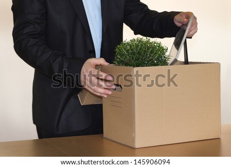 Fired man in a black suite pack his personal stuff into a brown cardboard box after