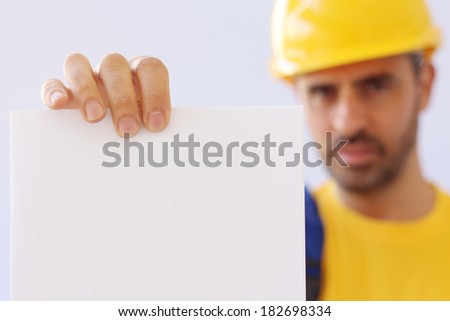 Handsome young bearded workman in a yellow hardhat and matching t-shirt holding empty page document
