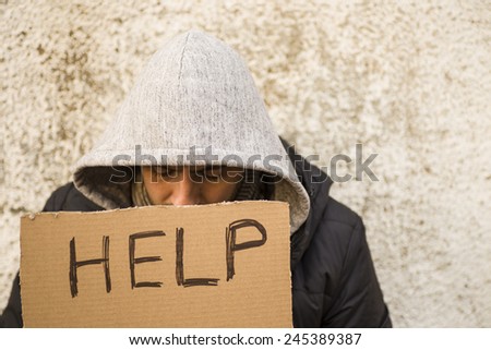 Close up of poor young guy with cartboard sign seeking help