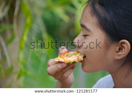 little Thai girl eating pizza. Thailand, a small girl with a dark skin eating pizza with a green background.