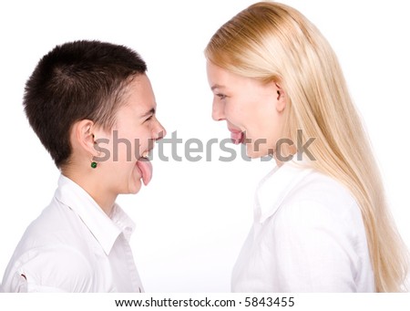 Close-cut brunette and long-haired blond stand face to face and to stick each other tongues out.