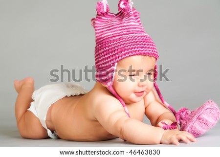 Smiling baby in pink cap laying on gray background