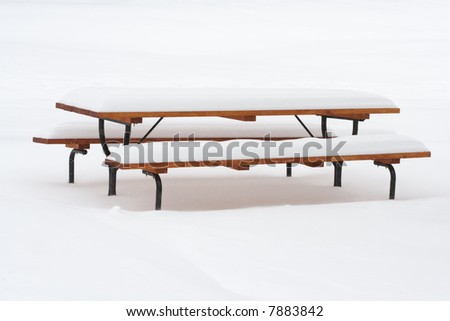 picnic table covering with thick snow over white snow background after a snowstorm