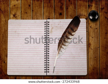 Open notebook and feather with ink bottle on a wooden board.