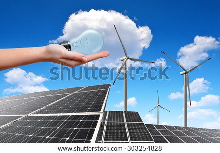 Hand holding lightbulb in the background solar energy panels and wind turbines