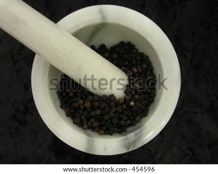 A pestal & mortar with black peppercorns on a black background.