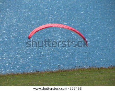 The parachute of a para-glider with green grass and a blue ocean behind.