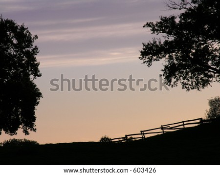 An empty sky with a silhouetted tree on each side of the picture, taken at dawn.