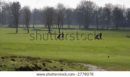 Two silhouettes of people with golf bags walking across the course on a winters morning