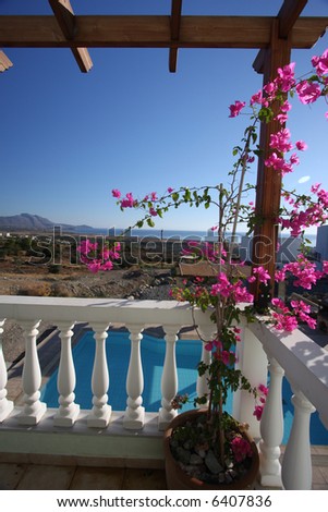 Vertical shot of a mediterranean balcony with pink flowers growing on it, the swimming pool beneath it and the sea in the distance. Taken in the Greek island of Rhodes