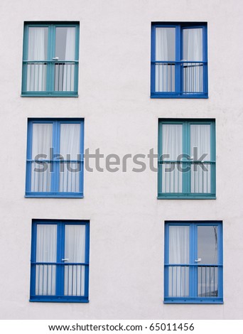 Blue patio doors and window, in a pattern on a white building wall.  Taken in vertical format.