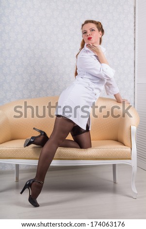 nurse in pinup style  leaned on the sofa and sends an air kiss