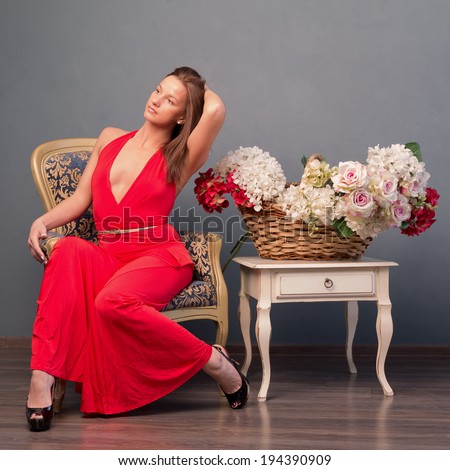 girl in red dress posing on  chair near vintage tables with basket of flowers