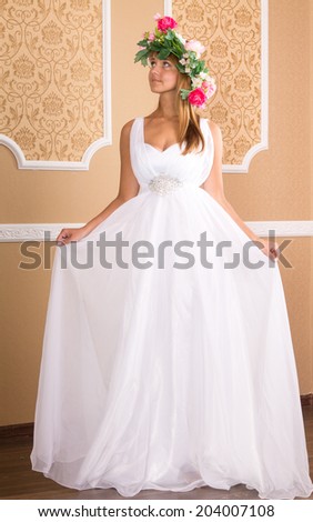 young woman  in white airy dress with wreath on his head on background of beige walls