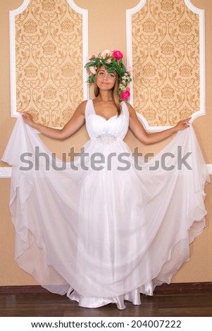 girl in white airy dress with wreath on his head on background of beige walls