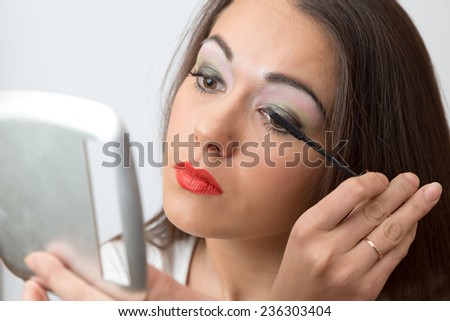 Brunette paints eyelashes mascara in the mirror on white background closeup