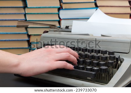 hand presses the button on the old typewriter on background of books