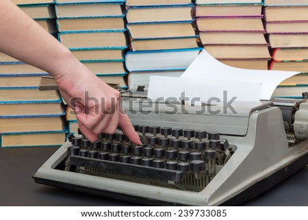 finger presses the button on the old typewriter on background of books