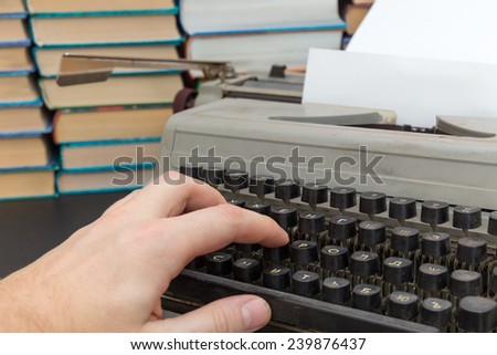 man\'s hand on an old typewriter in the background books