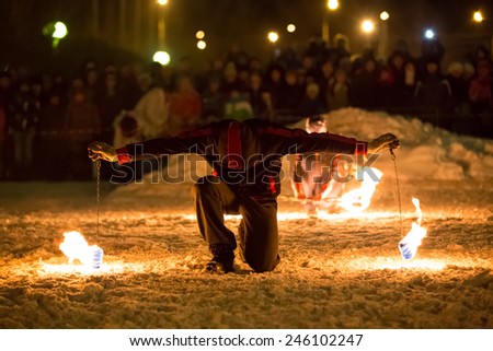 Perm, Russia - January 17, 2015. Man with two poi on chain in flame stands on knee in winter