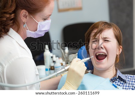 girl cries in chair at dentist. dentist holding drill