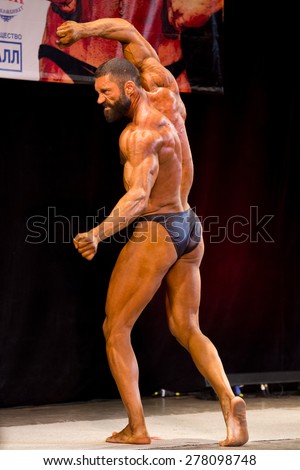 Izhevsk, Russia - April 18, 2015. Open championship of the Volga Federal District of bodybuilding and fitness bikini. Sun-Tanned bodybuilder with a beard is back and swing show biceps