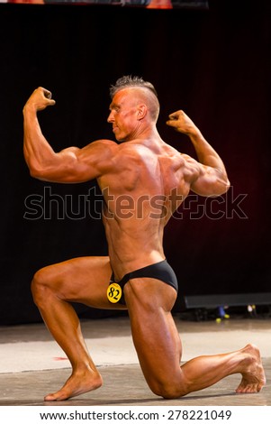 Izhevsk, Russia - April 18, 2015. Open championship of the Volga Federal District of bodybuilding and fitness bikini. Sun - tanned bodybuilder with a mohawk on his knees and shows biceps from back