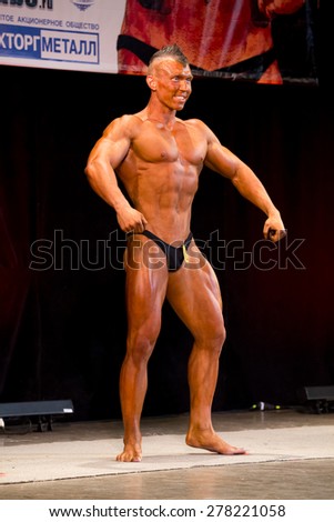 Izhevsk, Russia - April 18, 2015. Open championship of the Volga Federal District of bodybuilding and fitness bikini. Sun-tanned bodybuilder with a mohawk standing in frontal position