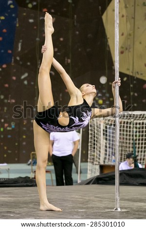 Perm, Russia - April 25, 2015. Championship Perm region at pole sport and dance. Girl in a black swimsuit with a white pattern makes a vertical split holding a pole