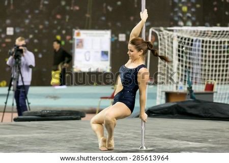 Perm, Russia - April 25, 2015. Championship Perm region at pole sport and dance. Smiling brunette in a black swimsuit stands on tiptoe holding pole