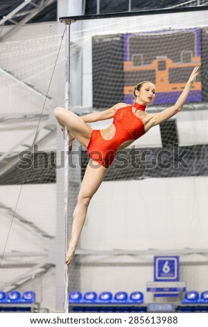 Perm, Russia - April 25, 2015. Championship Perm region at pole sport and dance. Serious brunette in a red  dance suit makes  element a hook knee