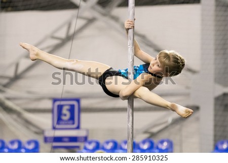Perm, Russia - April 25, 2015. Championship Perm region at pole sport and dance. Child in a black swimsuit with a blue pattern makes element Diva onpole split (elbow hold)