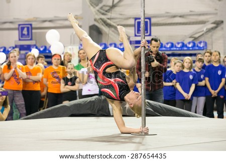 Perm, Russia - April 25, 2015. Championship Perm region at pole sport and dance.  blonde in a black swimsuit with a pink pattern makes element stand on the forearm near pole