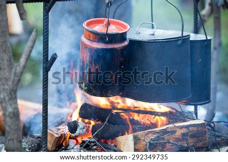 Two kettle and cans in soot hung over the fire in the campfire on fire