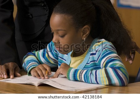 Student works in her workbook as teacher look over her shoulder