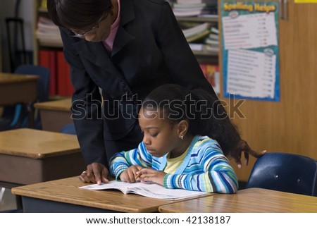 Teacher looking over students shoulder, as she works on her workbook in the class room