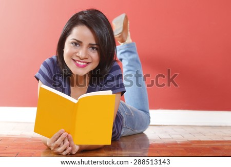 Beautiful young casual woman smiling  laying on the floor with a yellow book