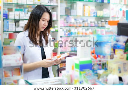 Young female pharmacist picking medicine and drugs from shelves in the drugstore