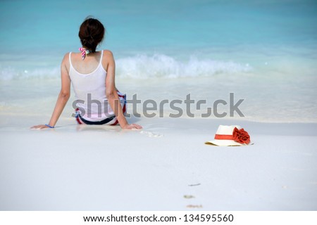 the hat is beside woman sitting on the beach and watching the sea