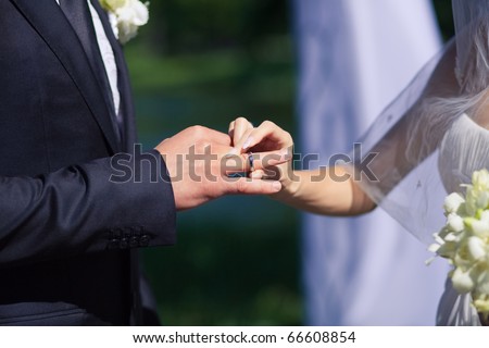 woman\'s hand putting a wedding ring on the grooms finger
