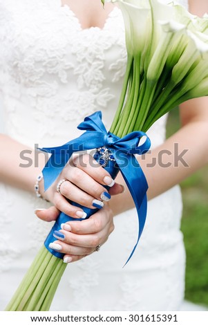 Bride with bouquet in hand, close-up, blue ribbon, flowers callas