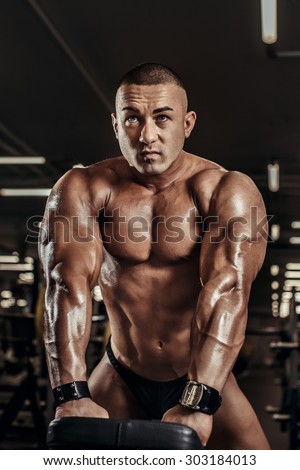 Handsome athletic man power training with dumbbells pumping muscle. Strong bodybuilder six pack, perfect ABS, shoulders, biceps, triceps and chest. Young adult bodybuilder doing weight lifting in gym.