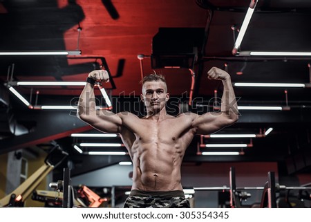Beautiful sport bodybuilder man on a diet, weight training with dumbbells pumping muscle.With six pack, perfect brakes, shoulders, biceps, triceps and chest.Young adult doing weight lifting at the gym
