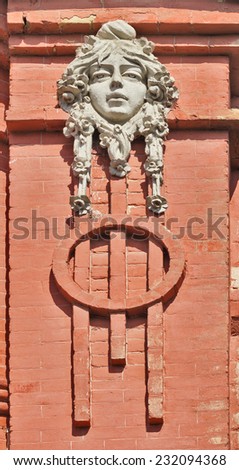 Gypsum architectural detail in the form of a mask on a red brick wall.