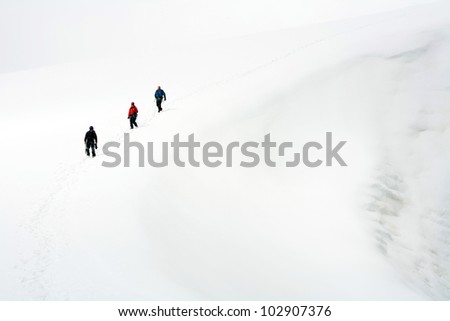 Team of three alpinists climbing a mountain during foggy weather